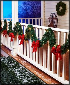 christmas wreaths on the front porch decorated with red bows and lights are hanging from the railing