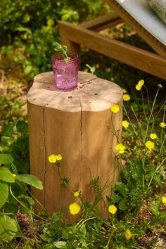 a pink glass sitting on top of a wooden stump in the grass next to flowers