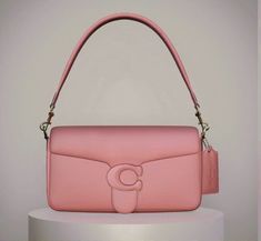 a pink handbag sitting on top of a white table next to a gray wall