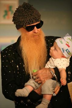 a man with a long beard holding a baby in his arms and wearing a hat