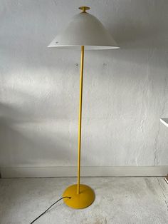 a yellow floor lamp sitting on top of a white wall next to a table and chair