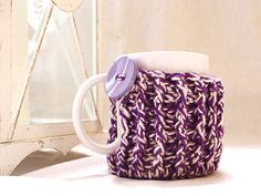 a purple and white knitted mug cozying next to a mirror with a button on it