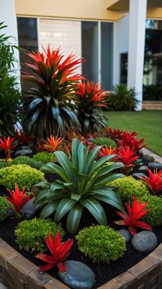 a garden with red flowers and green plants in front of a white building on the grass