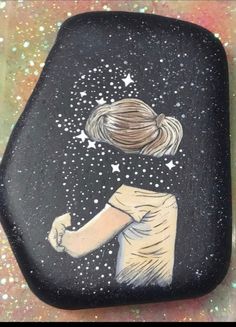 a painted rock with a drawing of a girl looking up at the stars