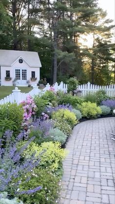 a white picket fence surrounded by lots of flowers and plants in front of a house