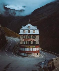 an old building sitting on the side of a road with mountains in the back ground