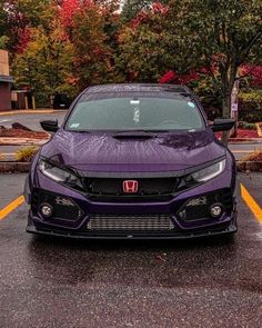 the front end of a purple car parked in a parking lot with trees and bushes behind it