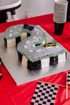 a cake shaped like the letter s on a table with race flags and plates in the background