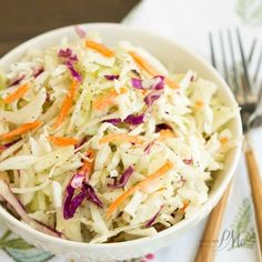 a white bowl filled with coleslaw on top of a table next to silverware