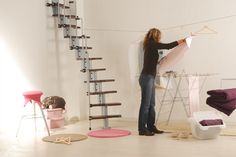 a woman is hanging clothes on a line in an empty room with chairs and ladders