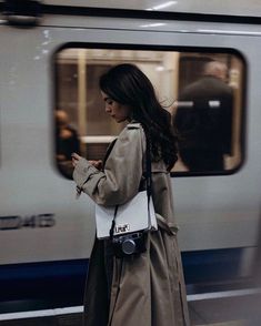 a woman is standing in front of a train and looking at her cell phone while waiting for the subway