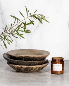 two bowls and a candle sit on a table next to a marble bowl with a plant in it