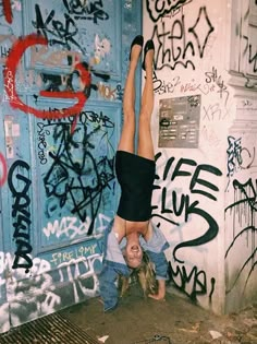 a person doing a handstand in front of a wall with graffiti on it