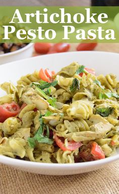 a white bowl filled with pesto pasta on top of a table next to tomatoes