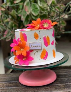 a white cake with orange and pink flowers on it sitting on a table next to a potted plant