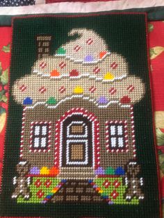 a close up of a cross stitched house on a table cloth with other items around it