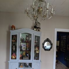 a white china cabinet with glass doors and chandelier hanging from it's ceiling