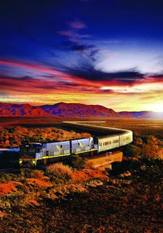 a train is traveling through the desert with mountains in the backgrouds at sunset