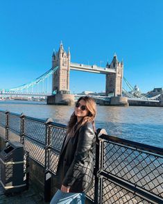 a woman standing on the side of a bridge next to a body of water with a bridge in the background