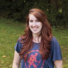 a woman with long red hair is standing in the grass smiling at the camera while holding a frisbee