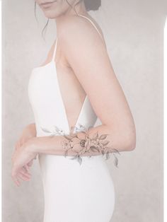 a woman wearing a white dress with flowers on her arm and the wrist is shown