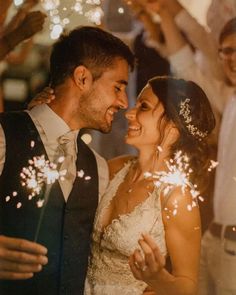 a newly married couple standing next to each other with sparklers in the air above them