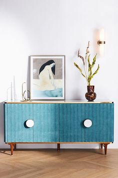 a blue sideboard with two white knobs on it and some plants in the corner