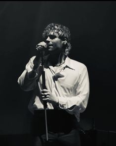 a man holding a microphone while standing in front of a black and white photo with his hand on the microphone