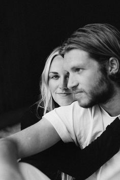 a black and white photo of a man and woman sitting next to each other looking at the camera