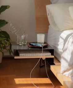 a table with some books and a cup on it in front of a bed next to a plant