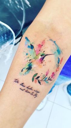 a watercolor tattoo on the arm of a woman's left arm, with words written in cursive writing