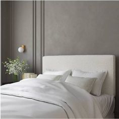 a bed with white sheets and pillows next to a vase with flowers on the headboard