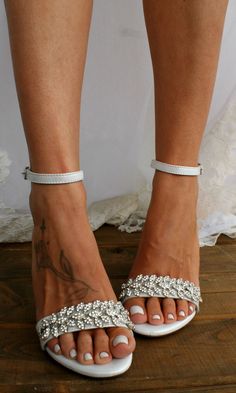 a close up of a person's feet wearing white sandals with silver beading