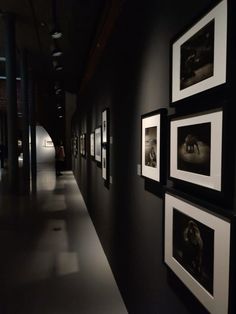 an empty hallway with black and white pictures on the wall, along with dark lighting