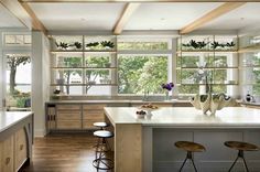 a large kitchen with wooden floors and white counter tops, along with two stools