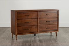 a wooden dresser sitting on top of a hard wood floor next to a white wall