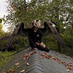 a woman sitting on top of a roof covered in leaves and an angel wings above her head