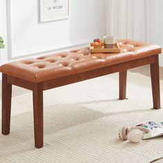 a brown leather bench sitting on top of a white rug next to a book and cup