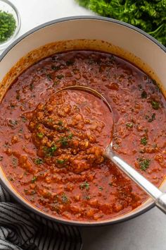 a large pot filled with red sauce and garnished with parsley on the side