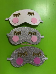 three sleeping masks with pink noses and gold eyelashes on green background, one has eyes closed