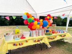 a table topped with lots of balloons next to a white tent filled with food and drinks