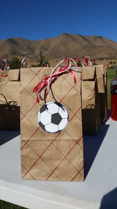 brown paper bags with a soccer ball and ribbon tied around them on a white table