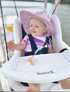 a baby wearing a pink hat and sitting in a white highchair on a boat