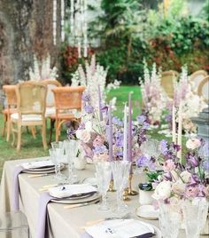 the table is set with purple and white flowers, candles, and place settings for dinner