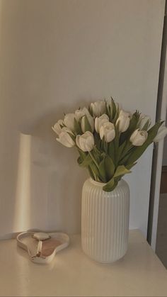 a white vase filled with flowers sitting on top of a table next to a pair of shoes