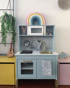 a toy kitchen with sink, stove and cupboards in the corner next to a potted plant