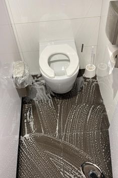 a white toilet sitting on top of a bathroom floor next to a roll of toilet paper