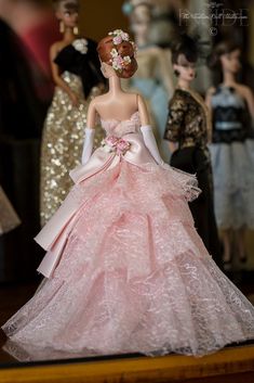 a barbie doll wearing a pink dress with flowers in her hair and other dolls behind her