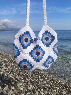 a crocheted bag hanging from a hook on the beach with water in the background