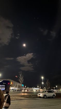 cars are parked on the side of the road at night with moon and stars in the sky